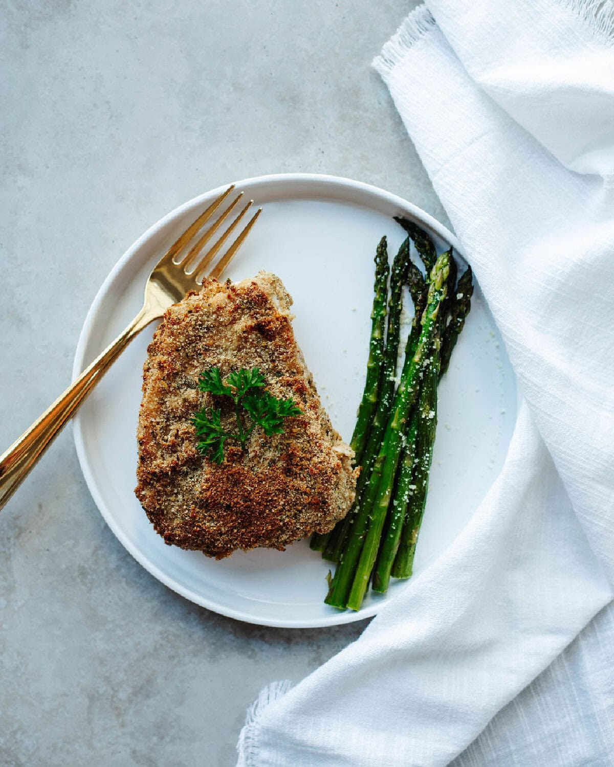 A plated pork chop with Ranch coating served with asparagus.