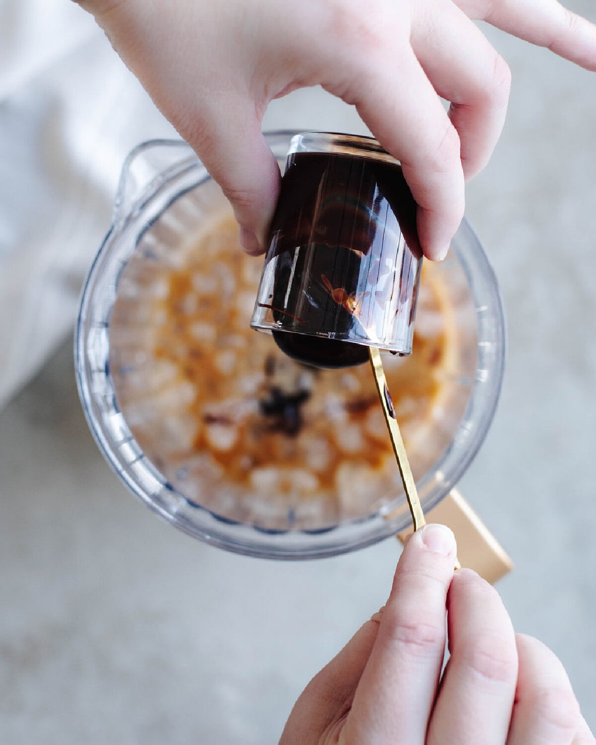 Chocolate syrup poured into a blender using a spoon.