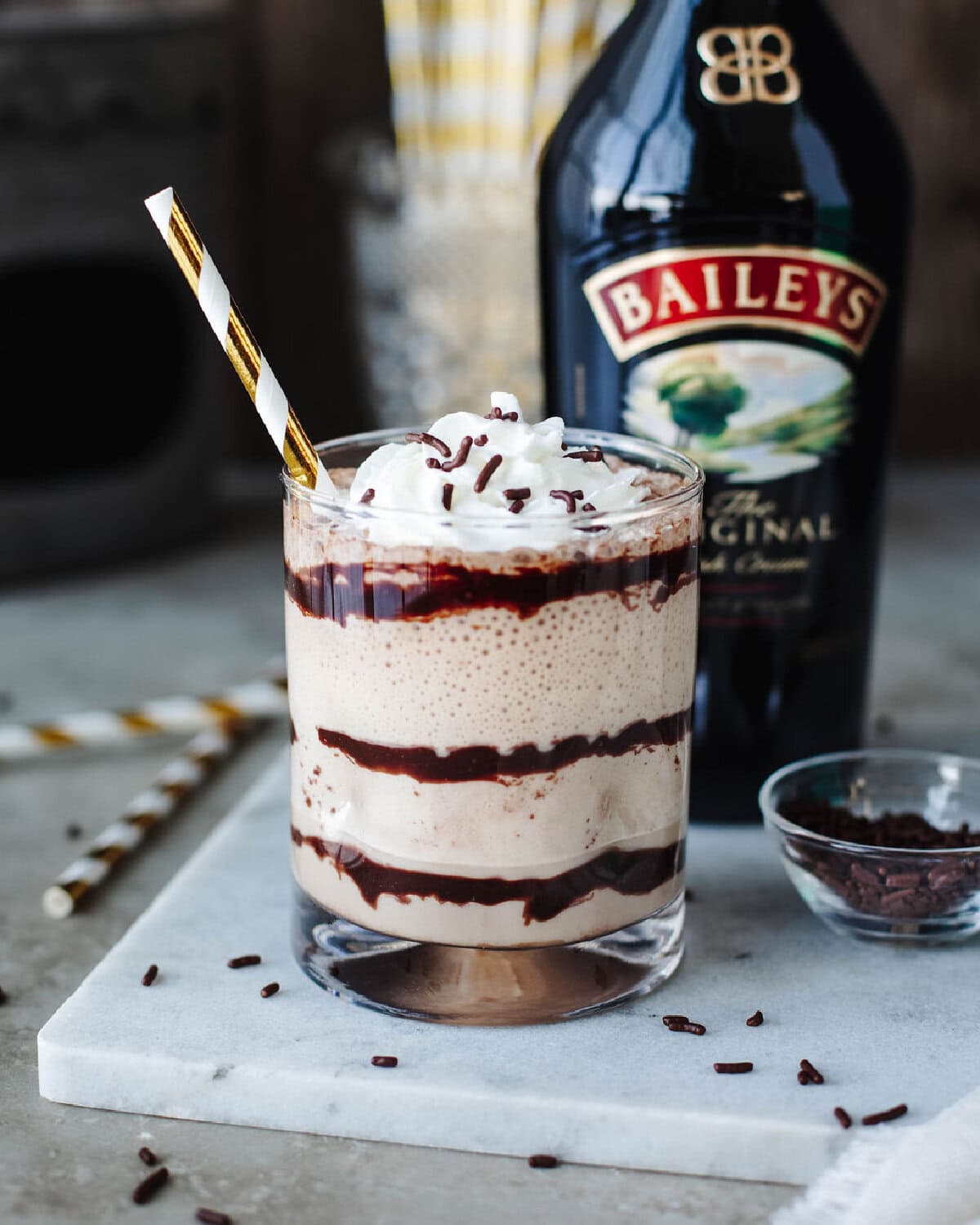 A glass of Baileys Frappuccino poured into a chocolate syrup drizzled cup and served with a straw.