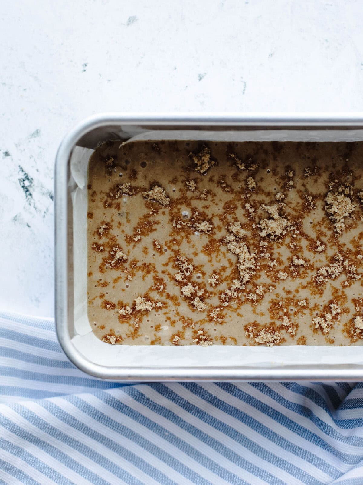 Bread batter spread evenly into a loaf pan with additional brown sugar on top.