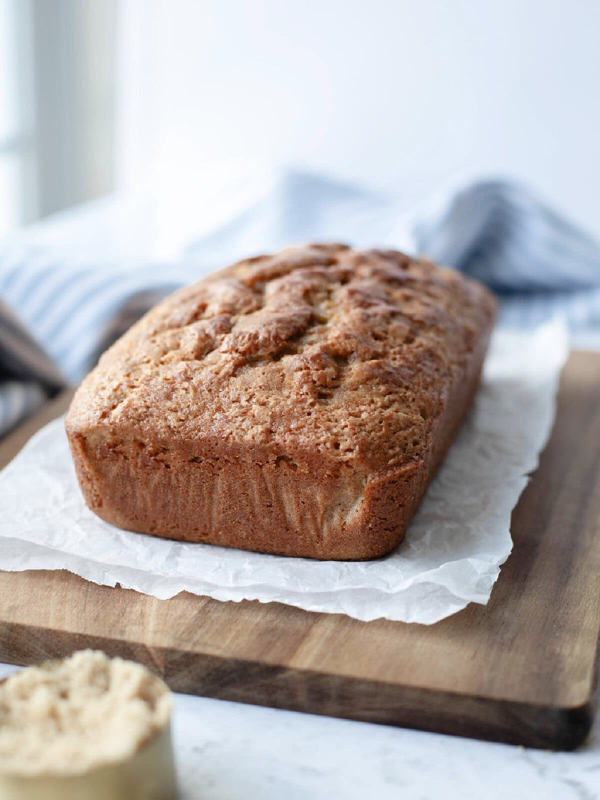 A baked loaf of brown sugar bread on a cutting board cooling.