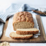 A sliced loaf of brown sugar quick bread ready to serve from a wood platter.