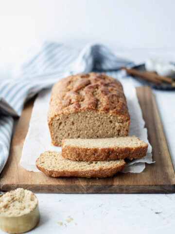 A sliced loaf of brown sugar quick bread ready to serve from a wood platter.