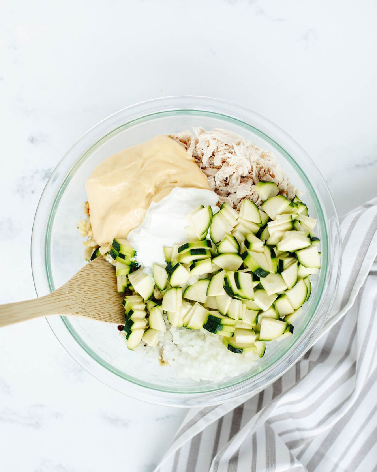 Zucchini, sour cream, cream of chicken, onion, and shredded chicken combined in a glass bowl.