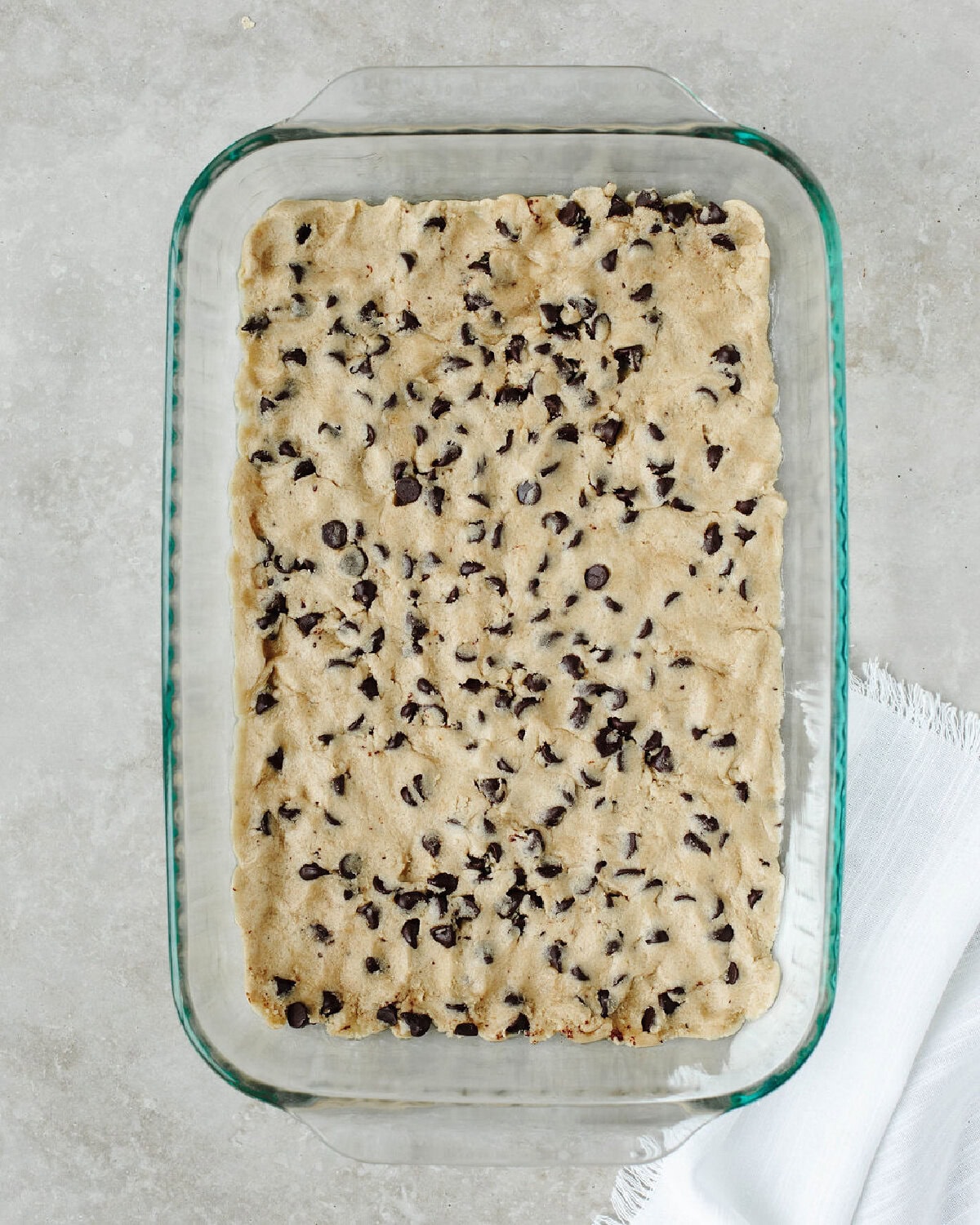 Chocolate chip cookie dough pressed evenly into a glass 9x13 baking pan.