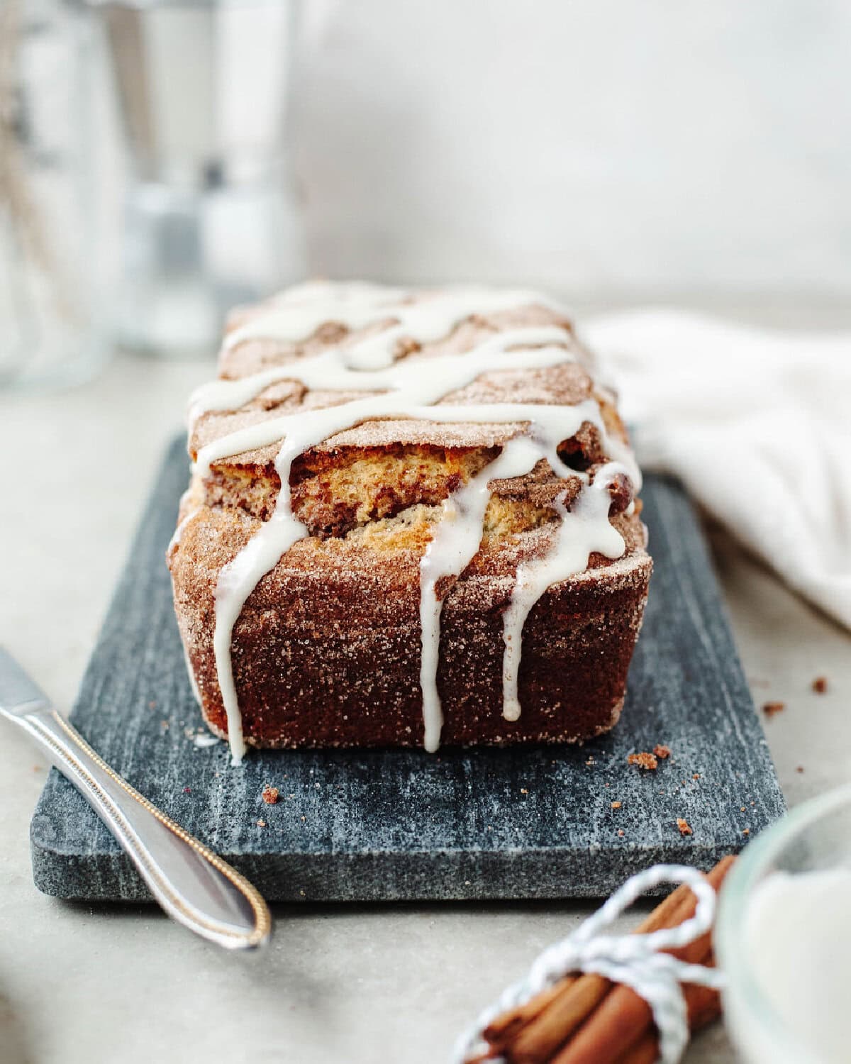 A baked loaf of cinnamon roll quick bread on a wood serving board and drizzled with a cream cheese frosting.