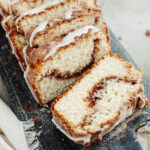 Sliced cinnamon bread with a cream cheese frosting on a wood board.