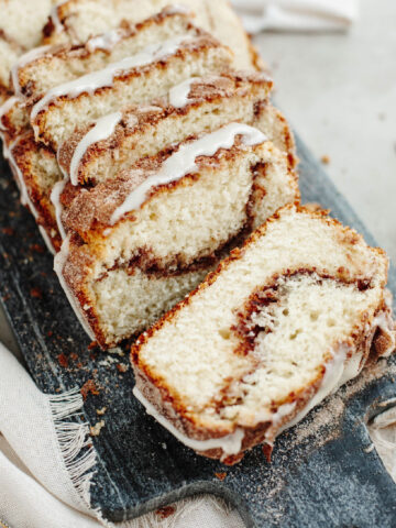 Sliced cinnamon bread with a cream cheese frosting on a wood board.