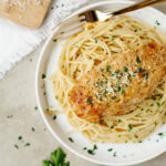 A chicken breast covered with a creamy mayonnaise sauce and served over pasta on a plate.