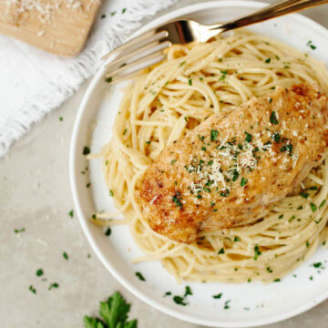 A chicken breast covered with a creamy mayonnaise sauce and served over pasta on a plate.