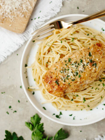 A chicken breast covered with a creamy mayonnaise sauce and served over pasta on a plate.