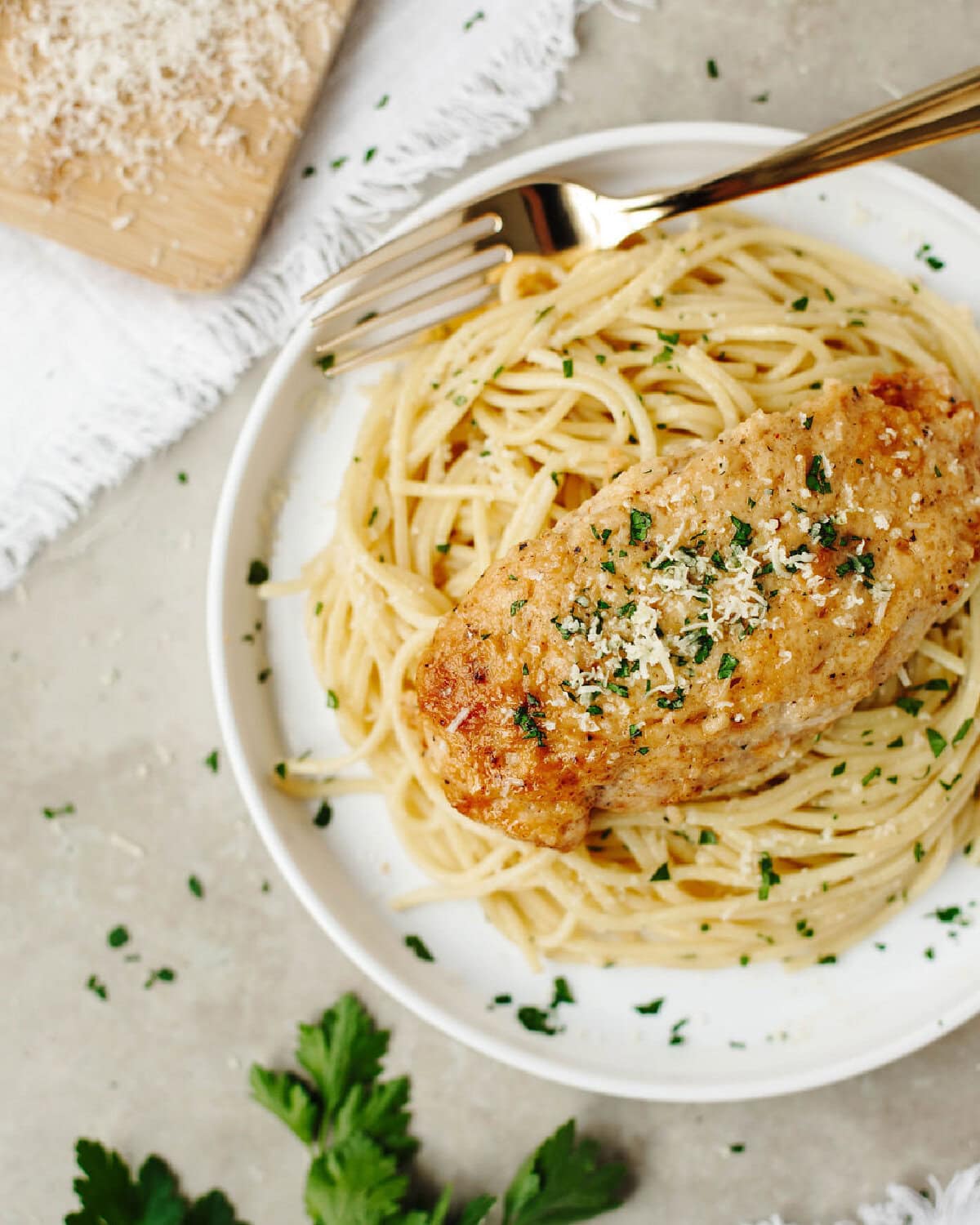 A chicken breast covered with a creamy mayonnaise sauce and served over pasta on a plate.