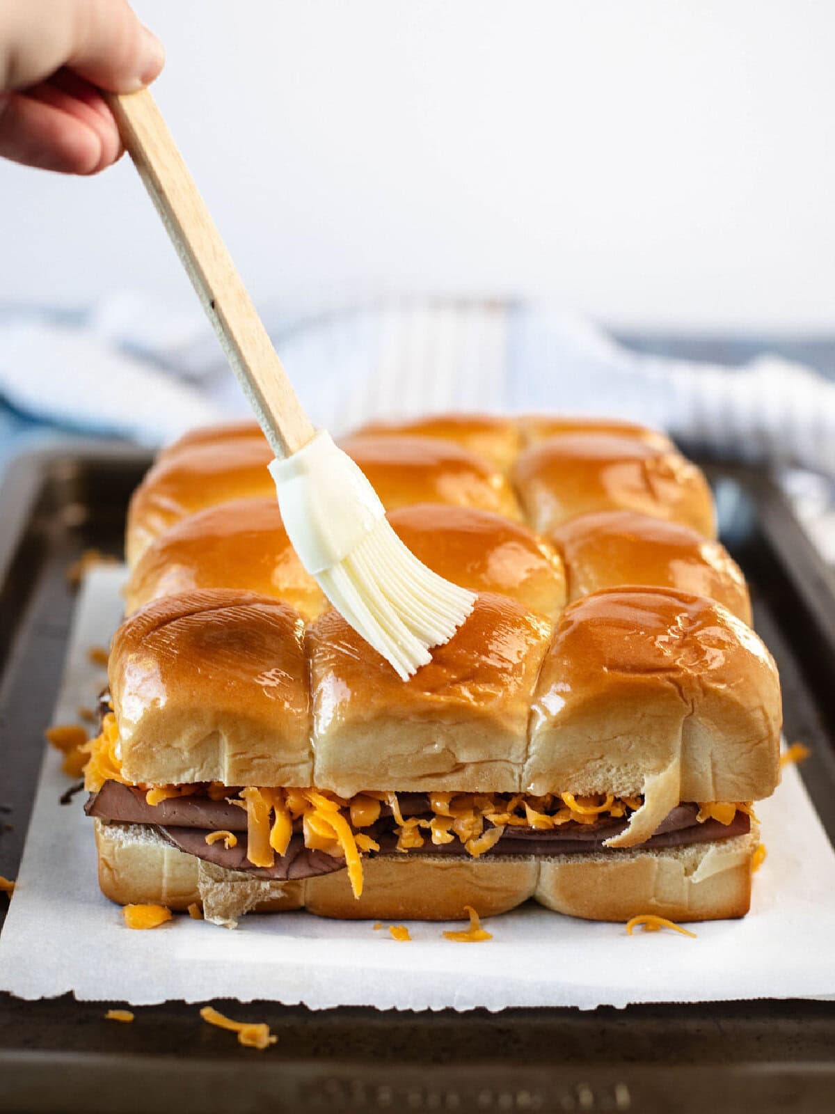 A pastry brush brushing melted butter on top of slider buns.