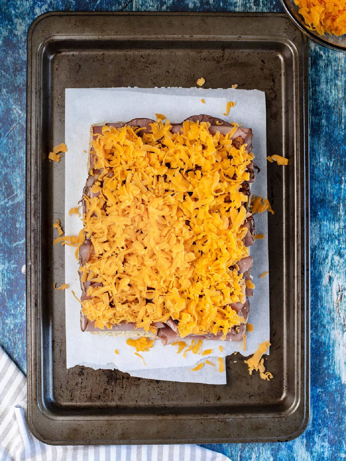 Shredded cheese on top of roast beef on a baking sheet.