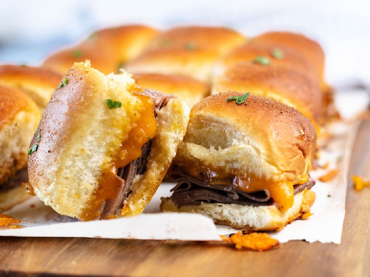 A close up of cheesy baked sliders with French onions and deli sliced roast beef.