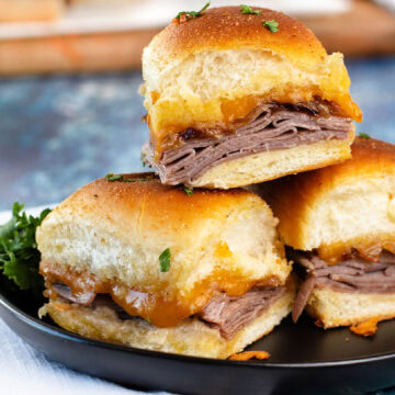 A stack of beef sliders with French onions on a black plate.