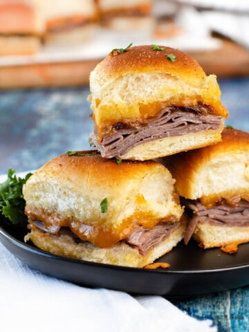 A stack of beef sliders with French onions on a black plate.