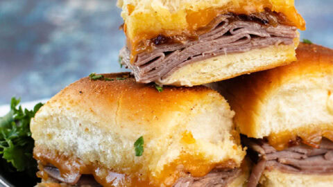 A stack of beef sliders with French onions on a black plate.