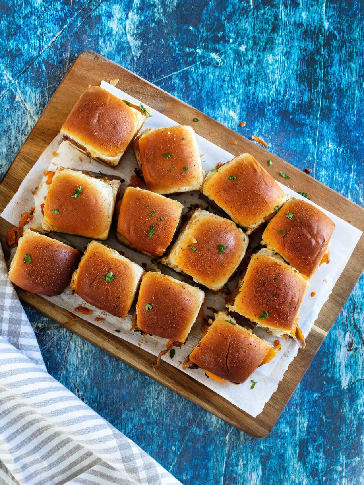 French Onion beef sliders baked and served on a wood platter.