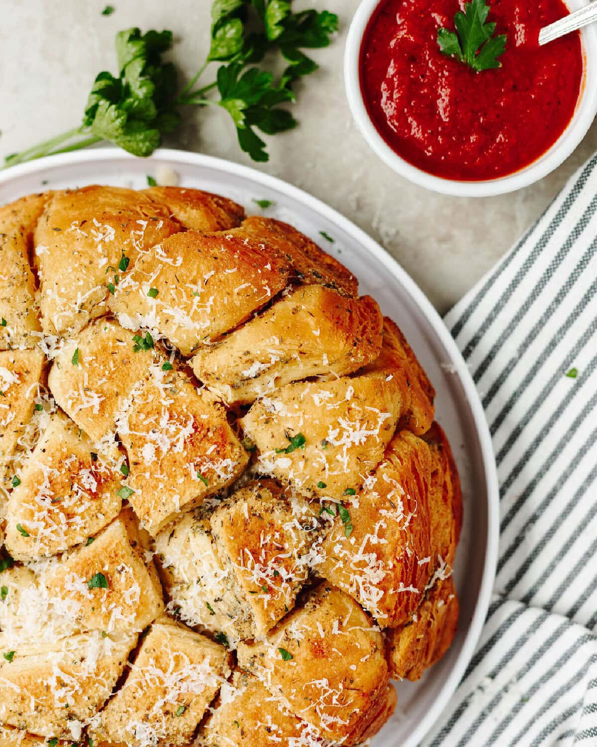 Top view of cheesy garlic pull apart bread on a white plate with a side of marinara sauce.