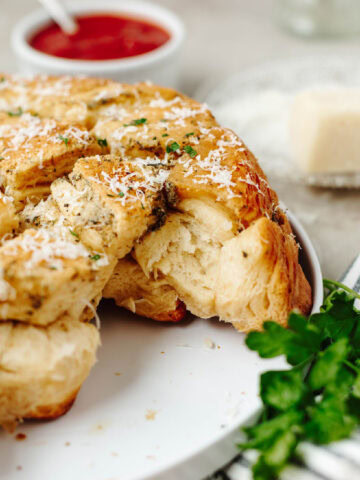 An up close look at garlic pull apart bread on a white plate with a side of marinara sauce.