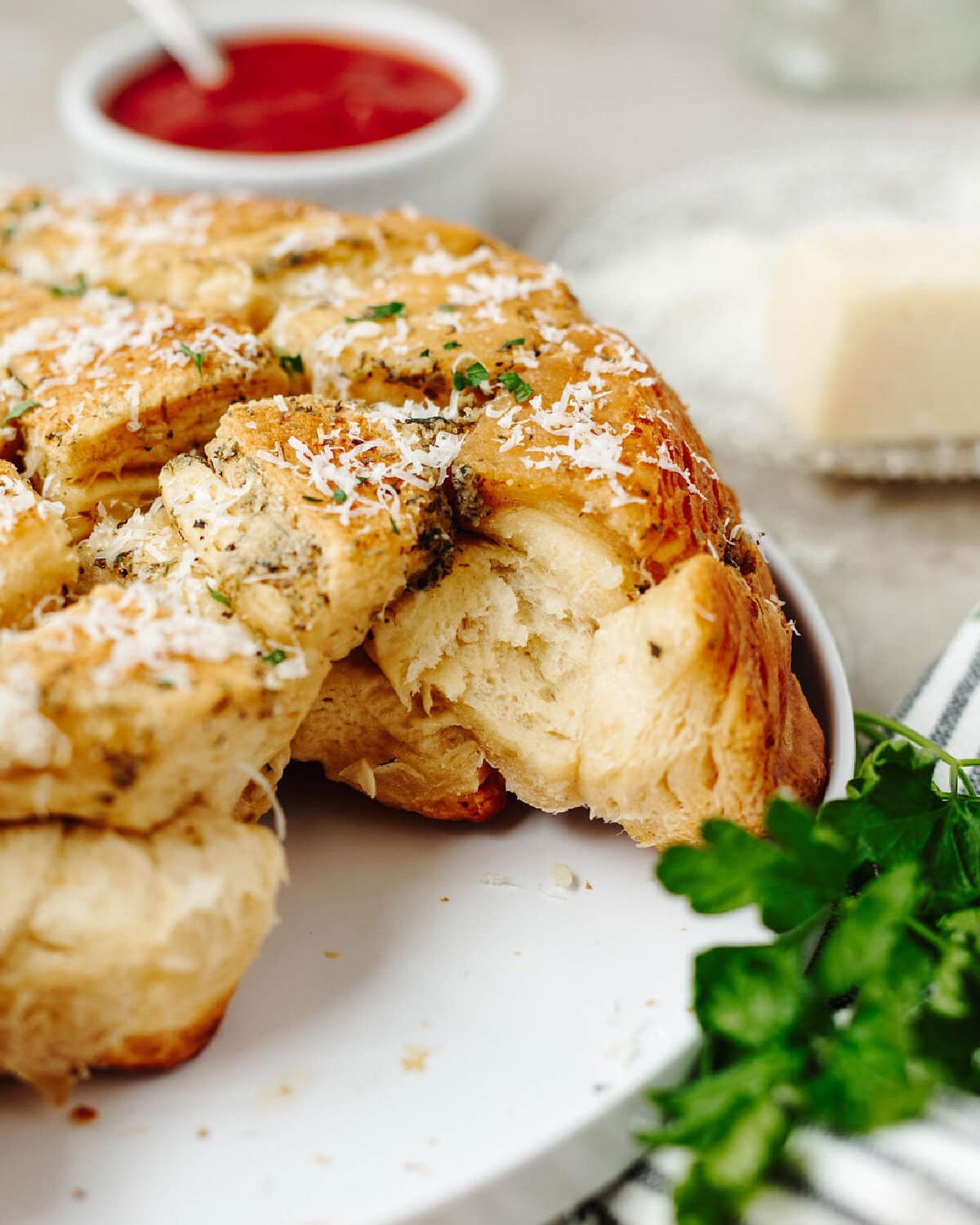 An up close look at garlic pull apart bread on a white plate with a side of marinara sauce.