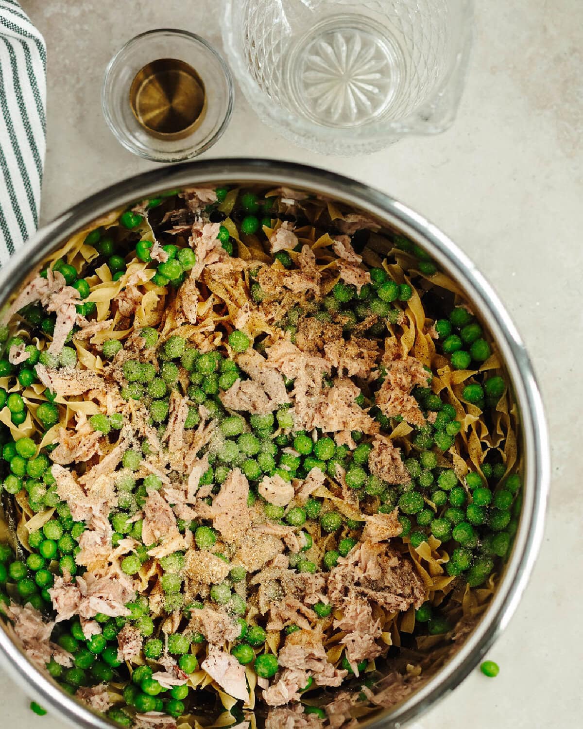Salt, pepper, and garlic powder added on top of egg noodles, tuna, and peas in an Instant Pot liner.