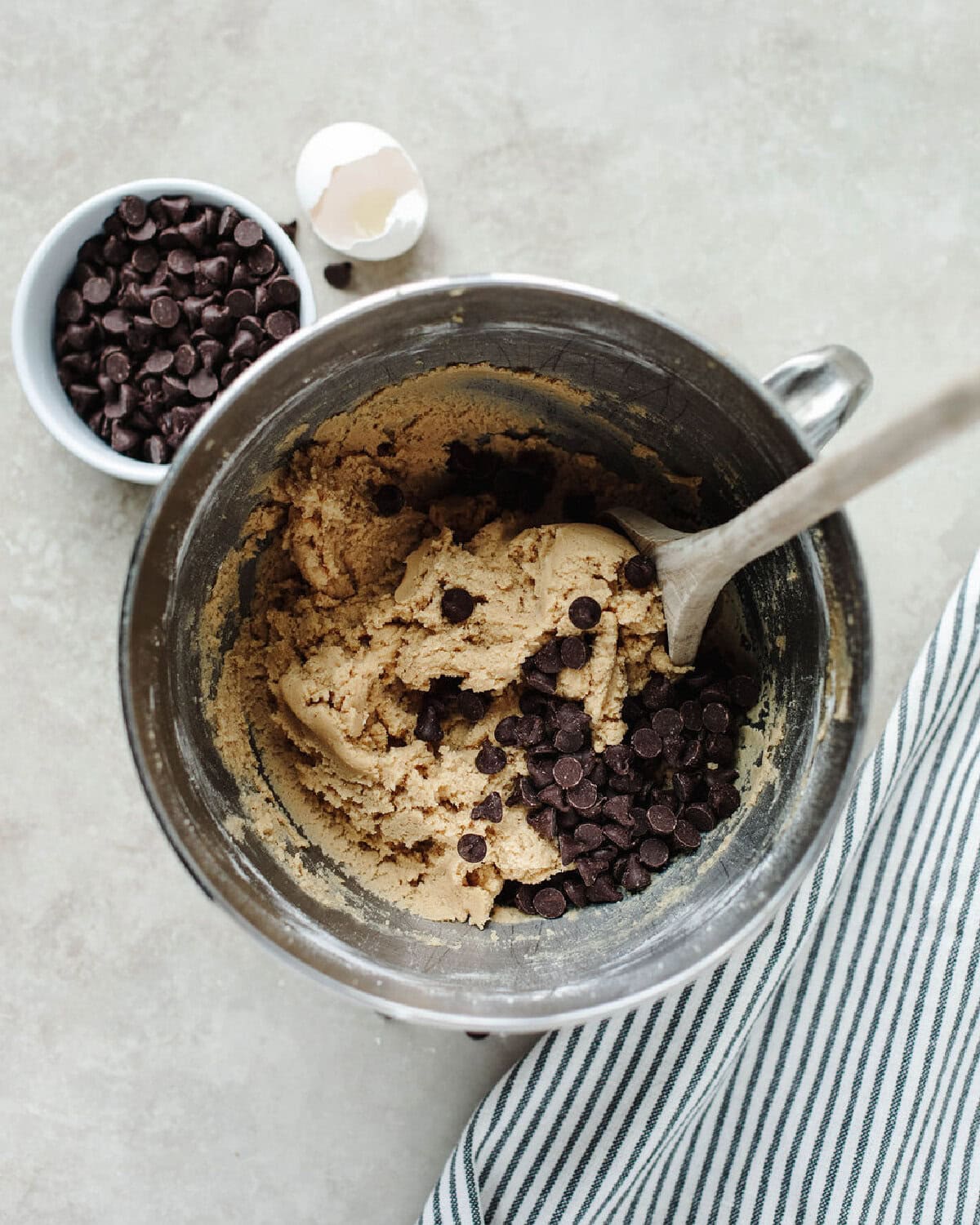 Chocolate chips folded into cookie dough in a mixing bowl using a wooden spoon.