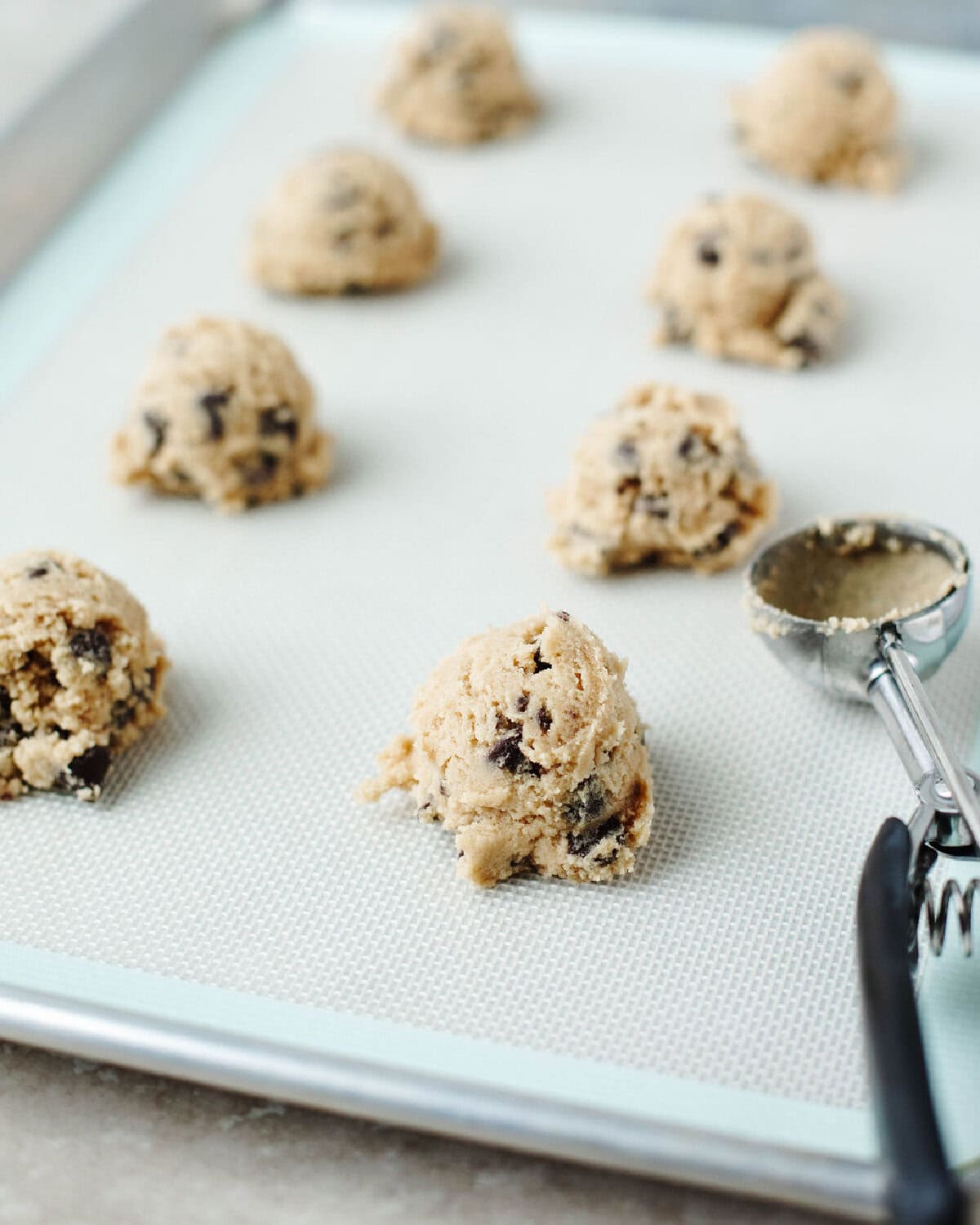 Cookie dough scooped onto a silicone lined baking sheet.