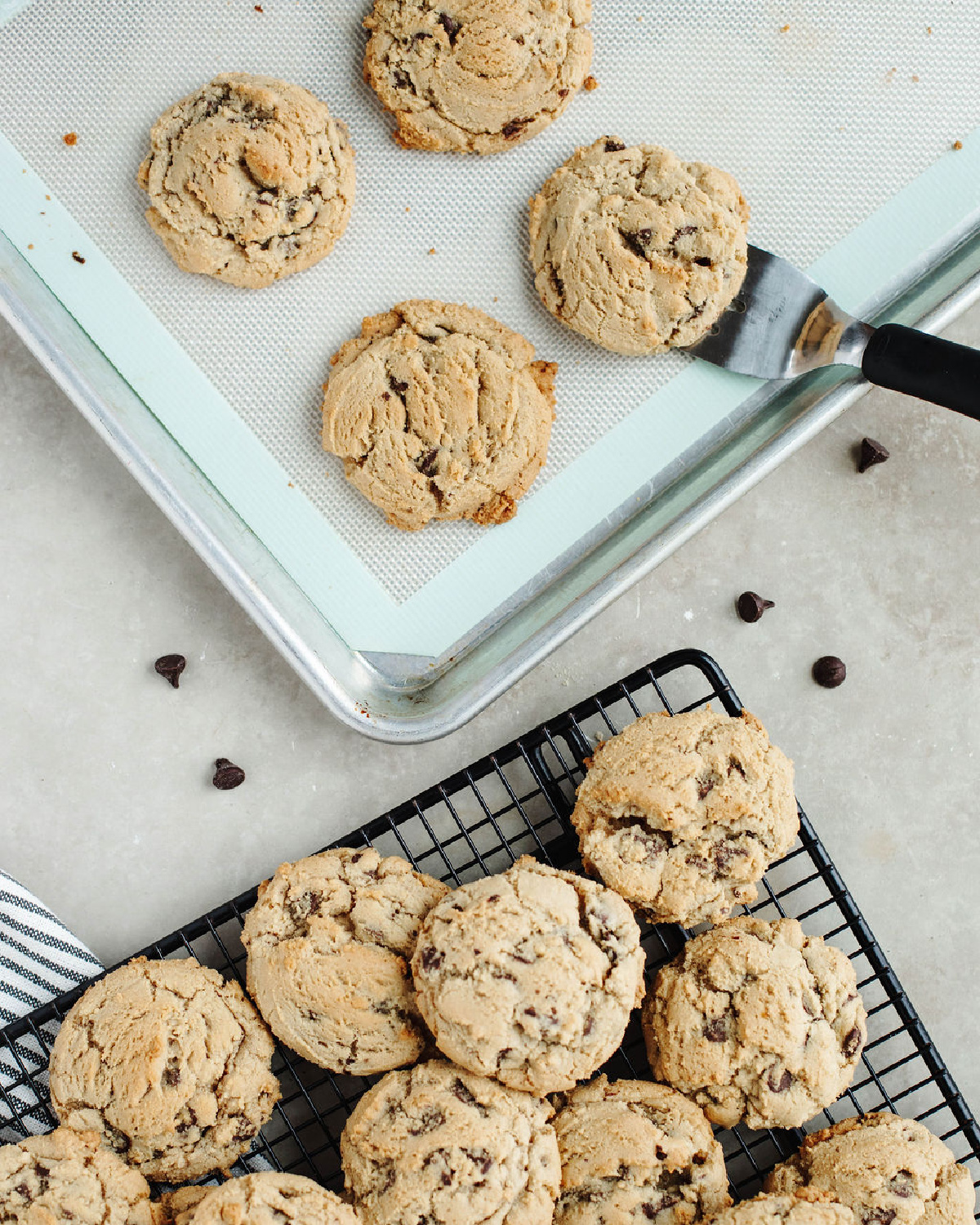 Cookies being scooped with a spatula from a cookie sheet to the wire cooling rack.