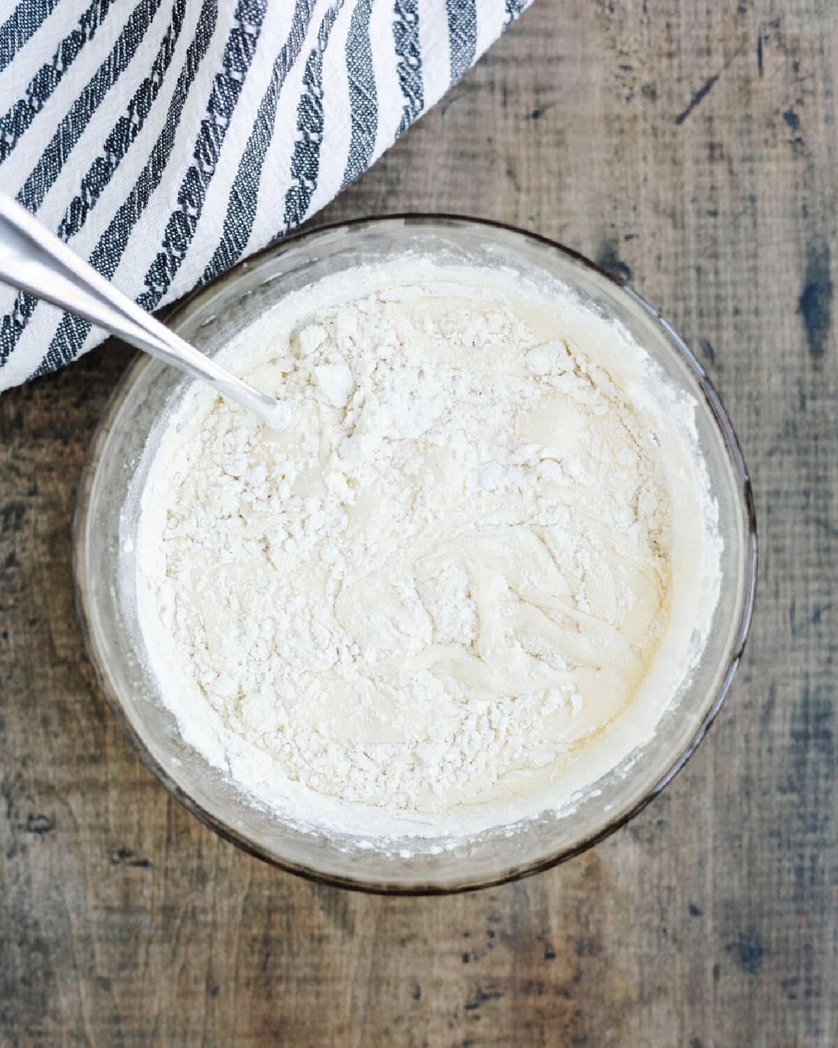 Flour stirred into cake batter in a glass mixing bowl.
