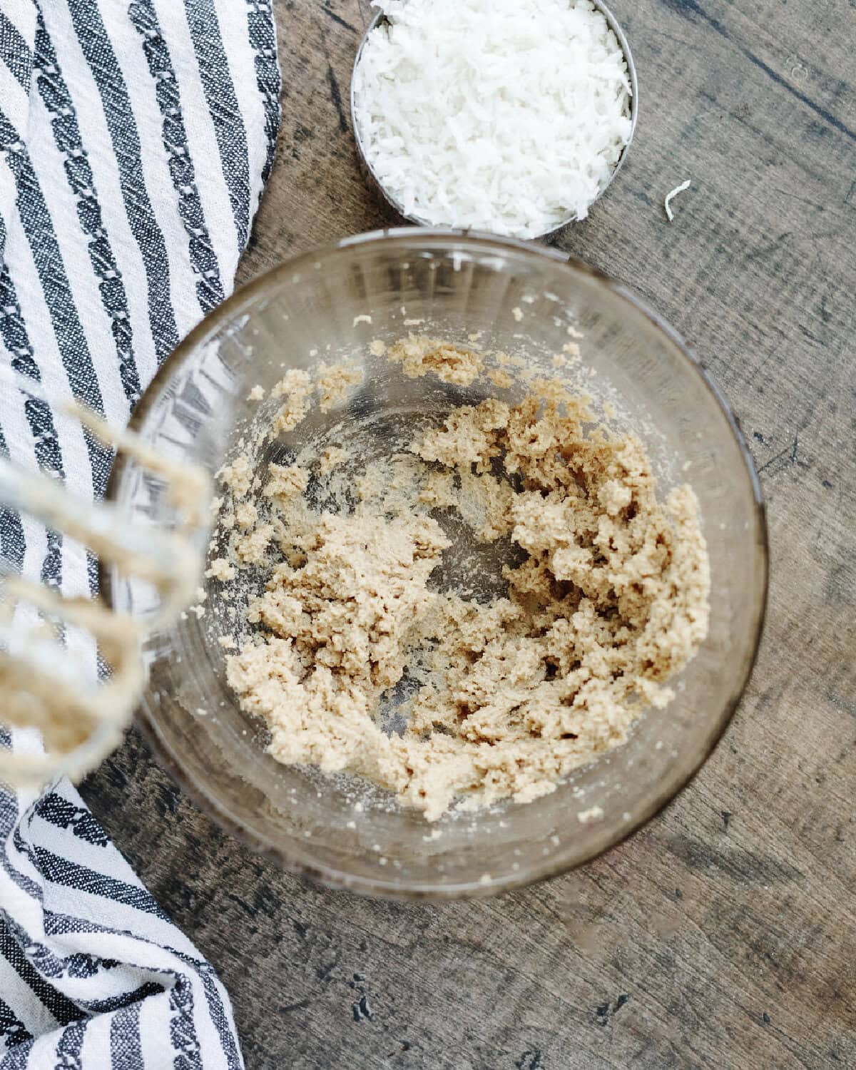 Flaky coconut frosting combined in a glass mixing bowl using an electric mixer.