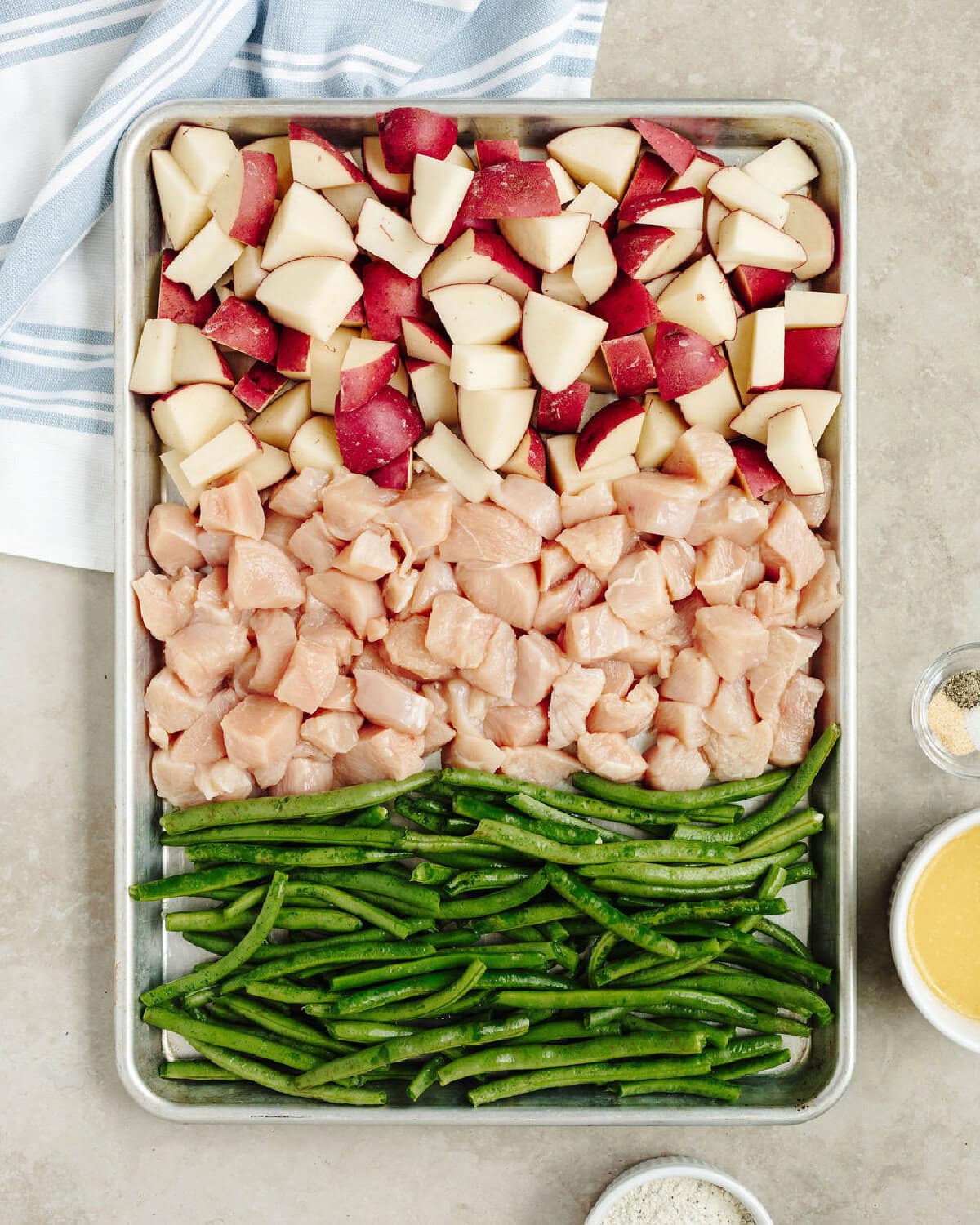 Diced potatoes, chicken, and green beans lined on a baking sheet.