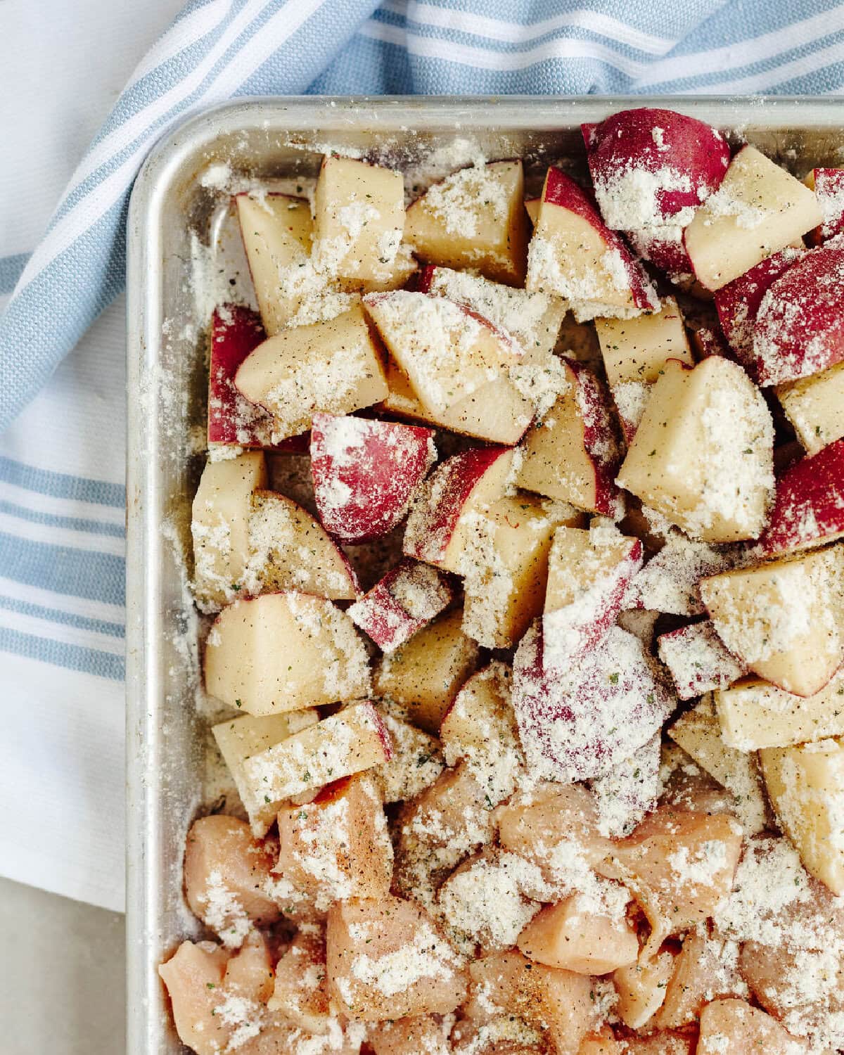 Ranch seasoning mix sprinkled on top of potatoes and chicken on a sheet pan.