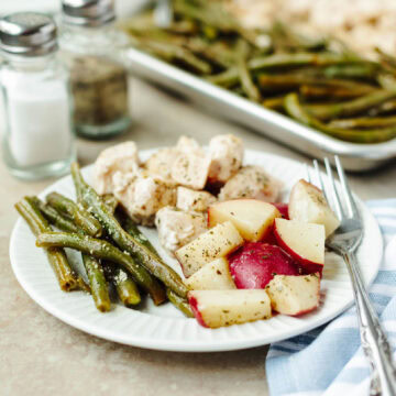 A white dinner plate with seasoned green beans, potatoes, and chicken ready to enjoy.