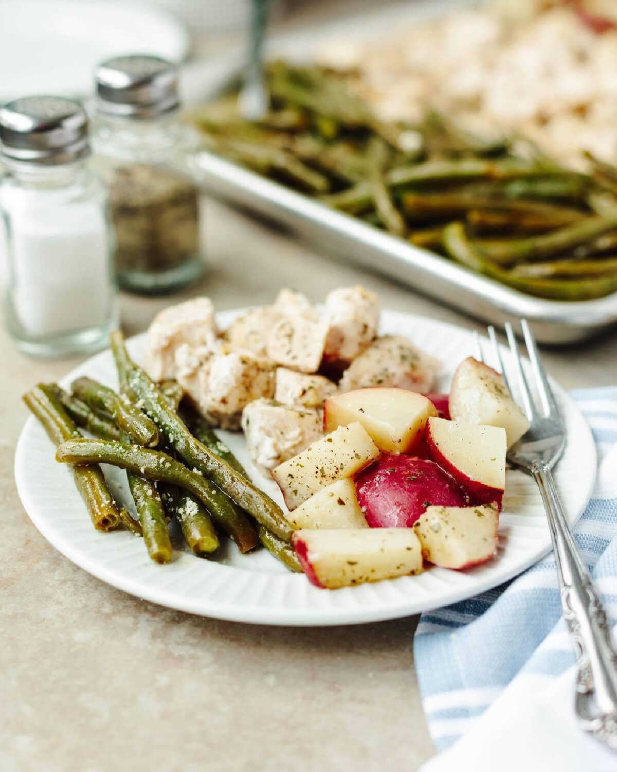 A white dinner plate with seasoned green beans, potatoes, and chicken ready to enjoy.