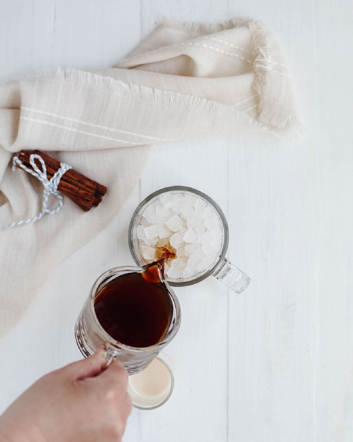Brewed coffee pouring over ice cubes in a glass mug.