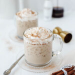 A glass mug filled with creamy RumChata iced coffee and topped with whipped cream and sprinkled cinnamon.