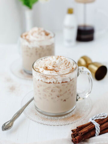 A glass mug filled with creamy RumChata iced coffee and topped with whipped cream and sprinkled cinnamon.