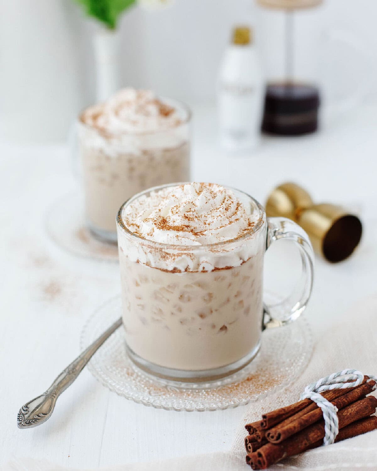A glass mug filled with creamy RumChata iced coffee and topped with whipped cream and sprinkled cinnamon.