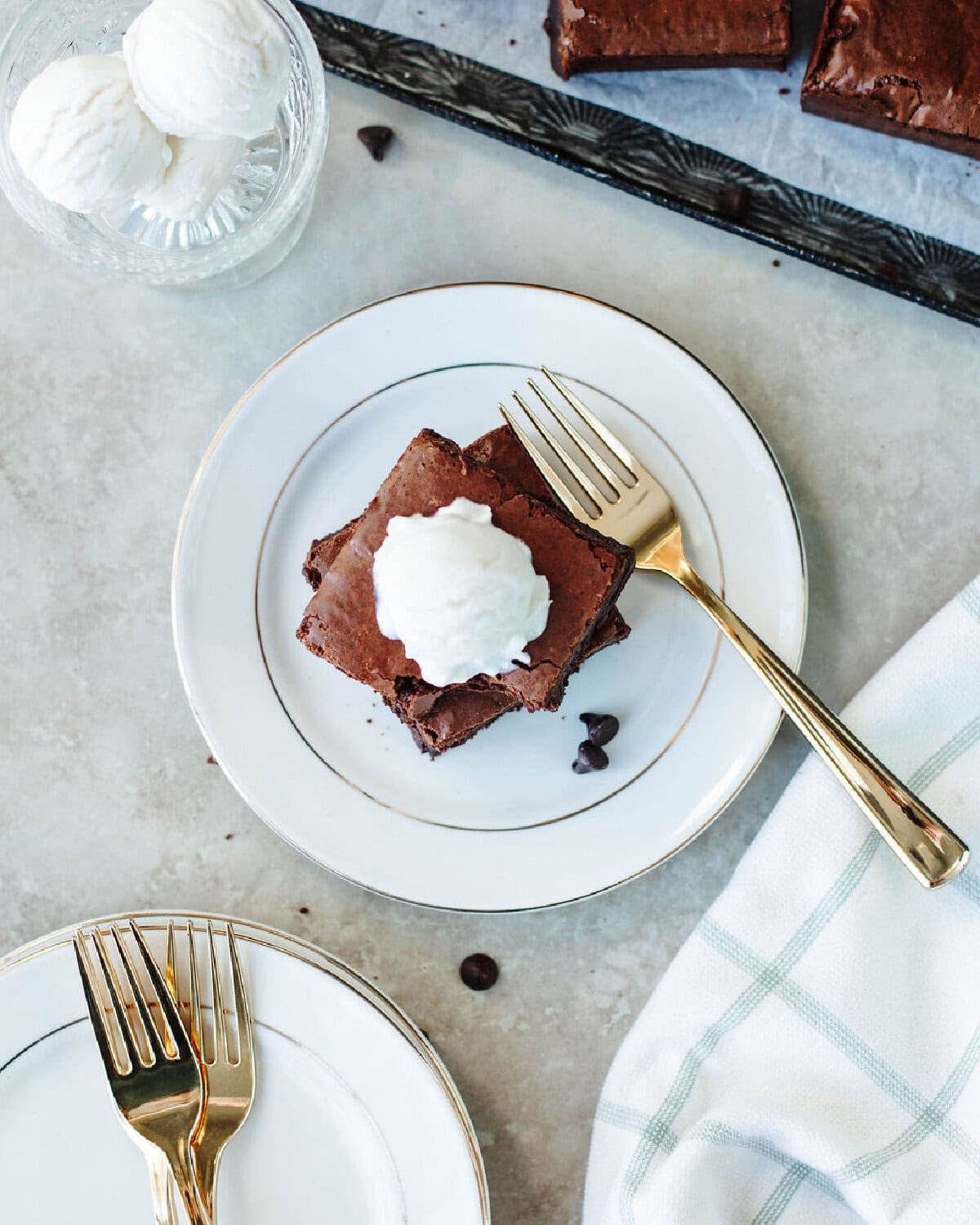 Two sourdough discard brownies on a white plate with a scoop of vanilla ice cream on top.