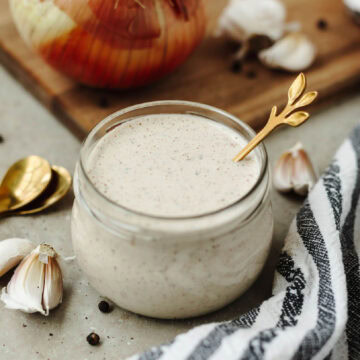 A white tangy BBQ sauce in a small glass jar with a spoon.