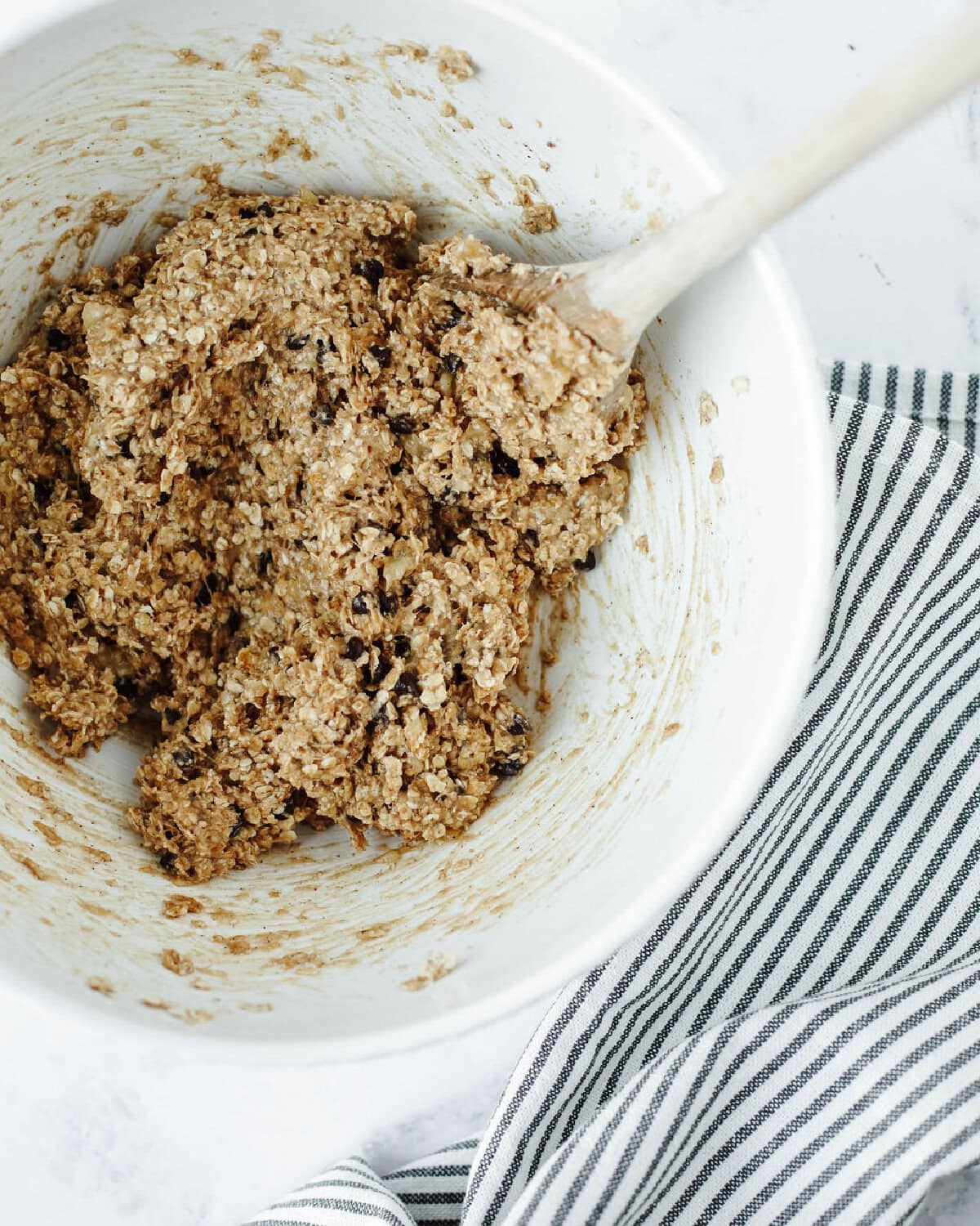 Cookie dough combined in a mixing bowl using a wood spoon.