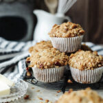 Stacked banana pecan muffins with paper liners on a wire serving tray.