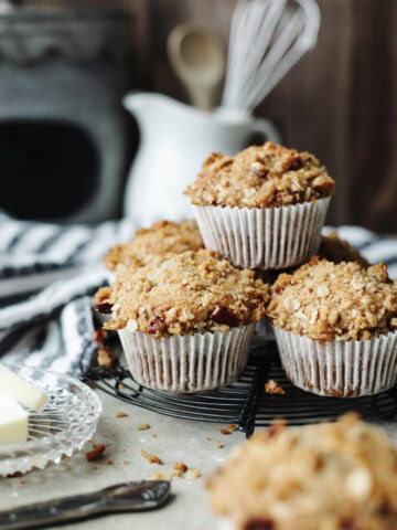 Stacked banana pecan muffins with paper liners on a wire serving tray.