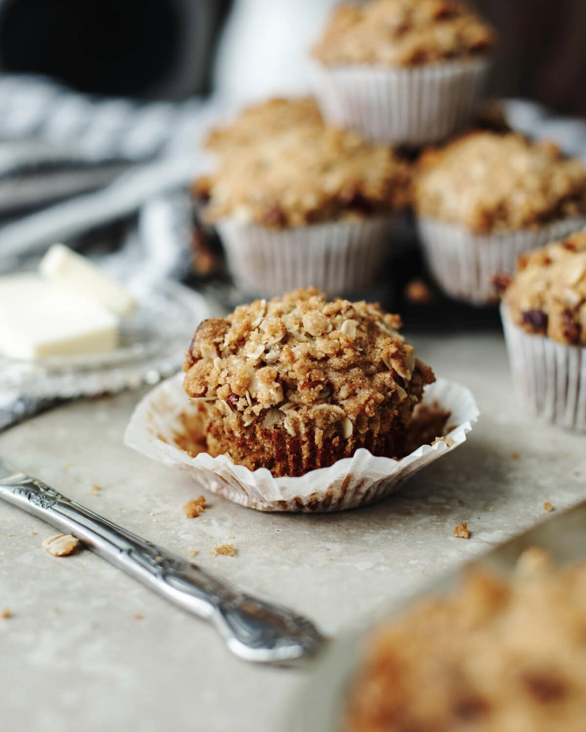 A crunchy oat topping on top of a banana muffin with a white paper liner.