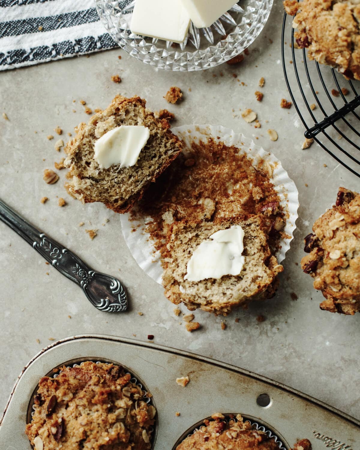 A spread of butter on top of a halved banana pecan muffin.