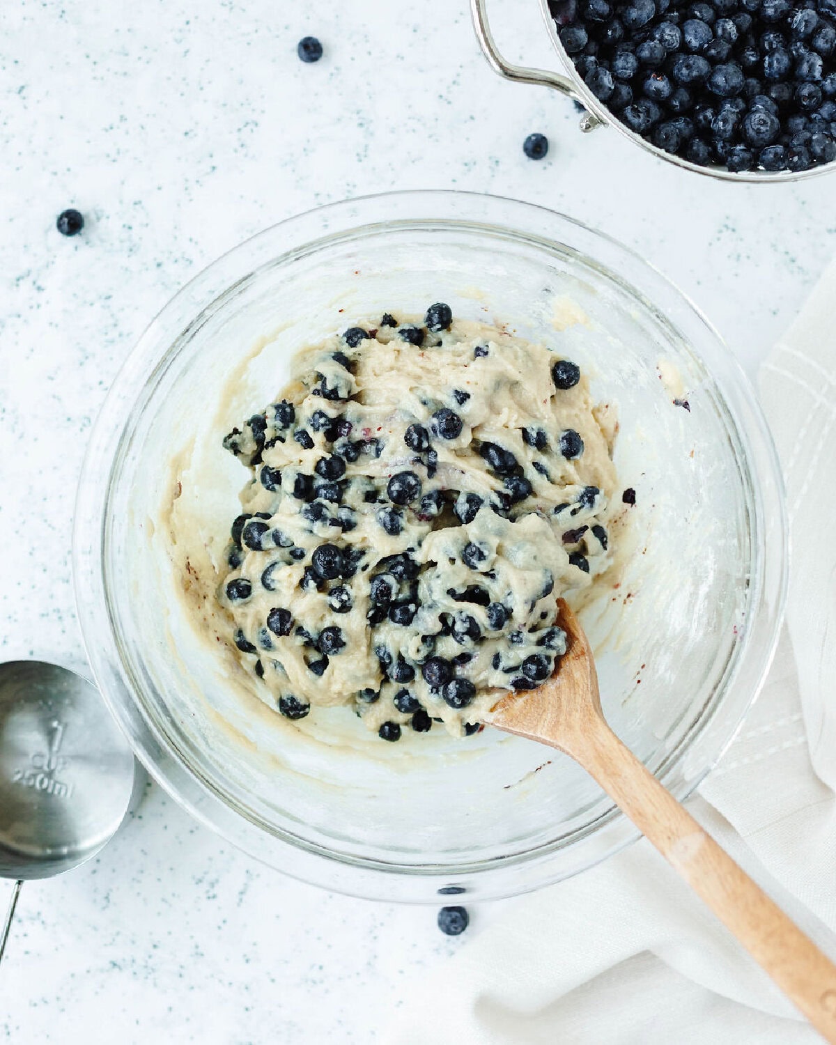Blueberries folded into batter using a wood spoon.
