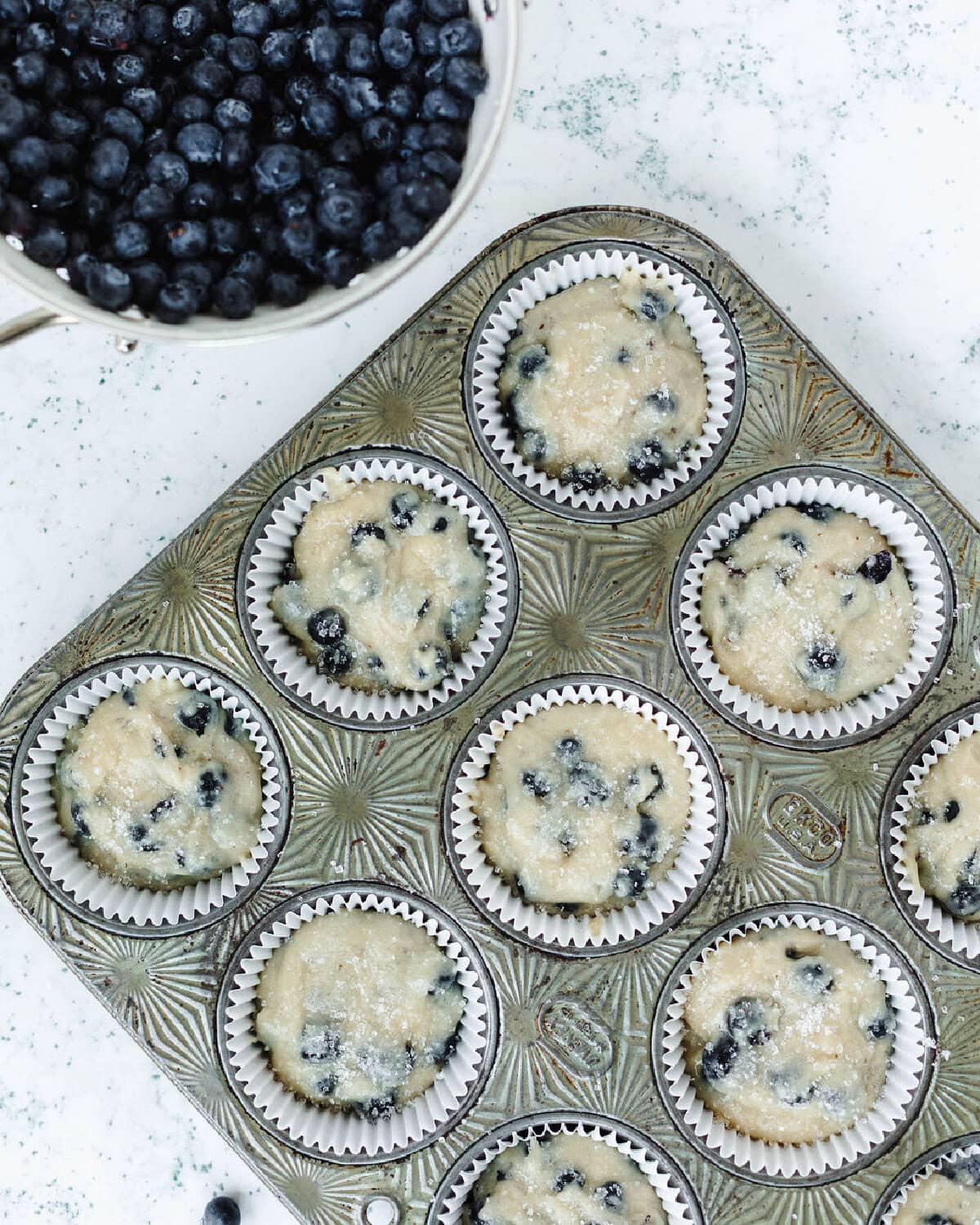 Muffin batter spread evenly into white paper liners and ready for the oven.