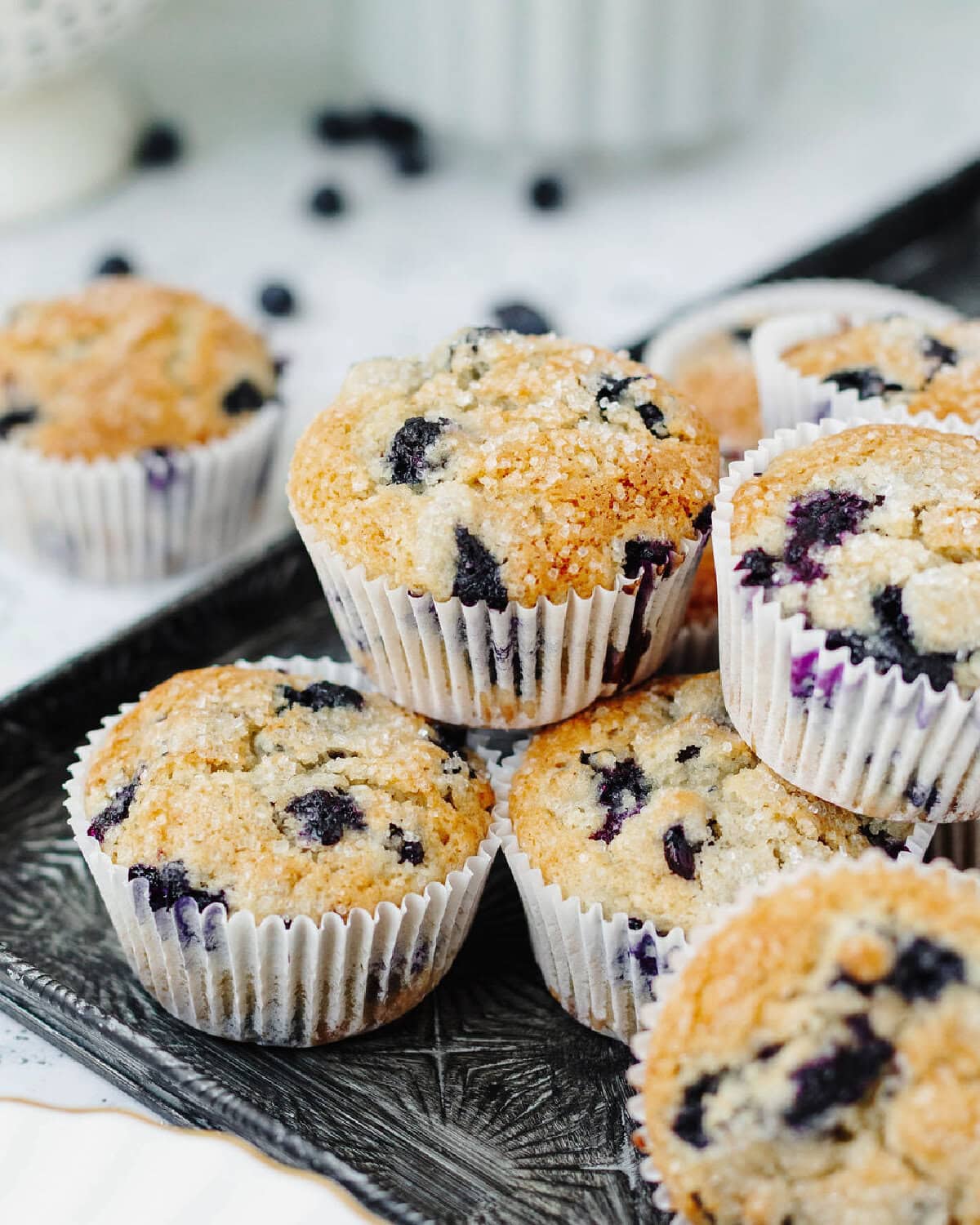 Fresh blueberry muffins with white paper liners stacked on a serving tray.